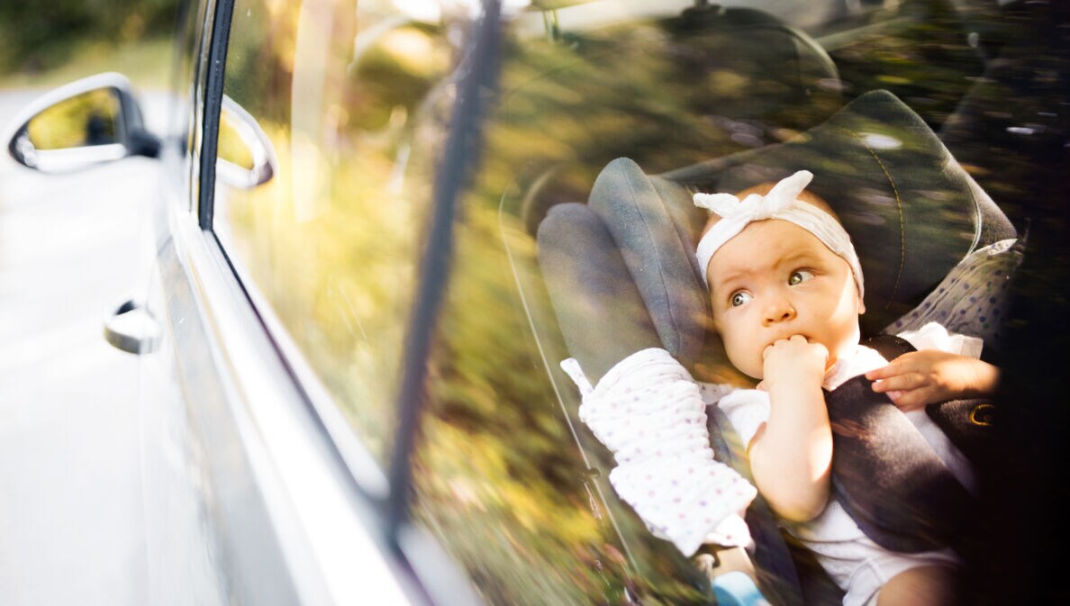 Kind sitzt auf dem Rücksitz eines Autos, hält ein Taschentuch und trägt eine weiße Bluse mit schwarzen Punkten.