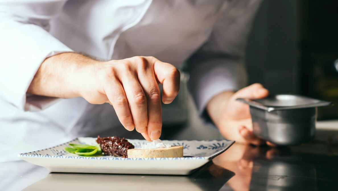 Hand eines Kochs, der einen Teller zubereitet.