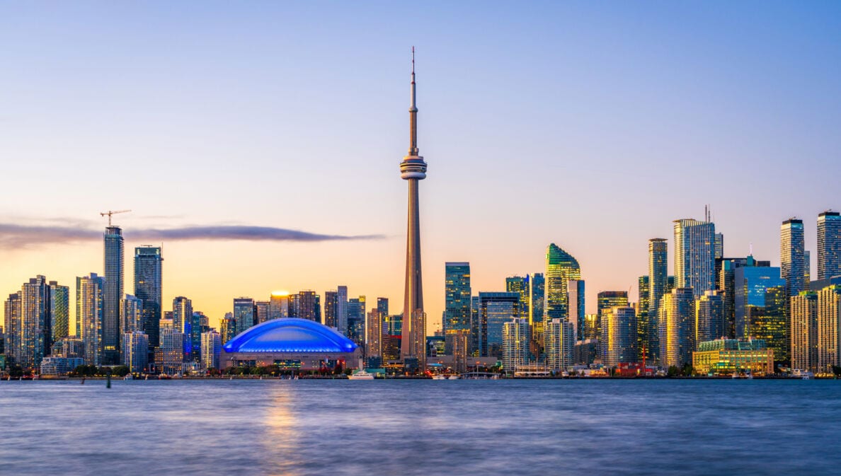 Skyline von Toronto mit Hochhäusern und Fernsehturm am Wasser im Abendlicht.