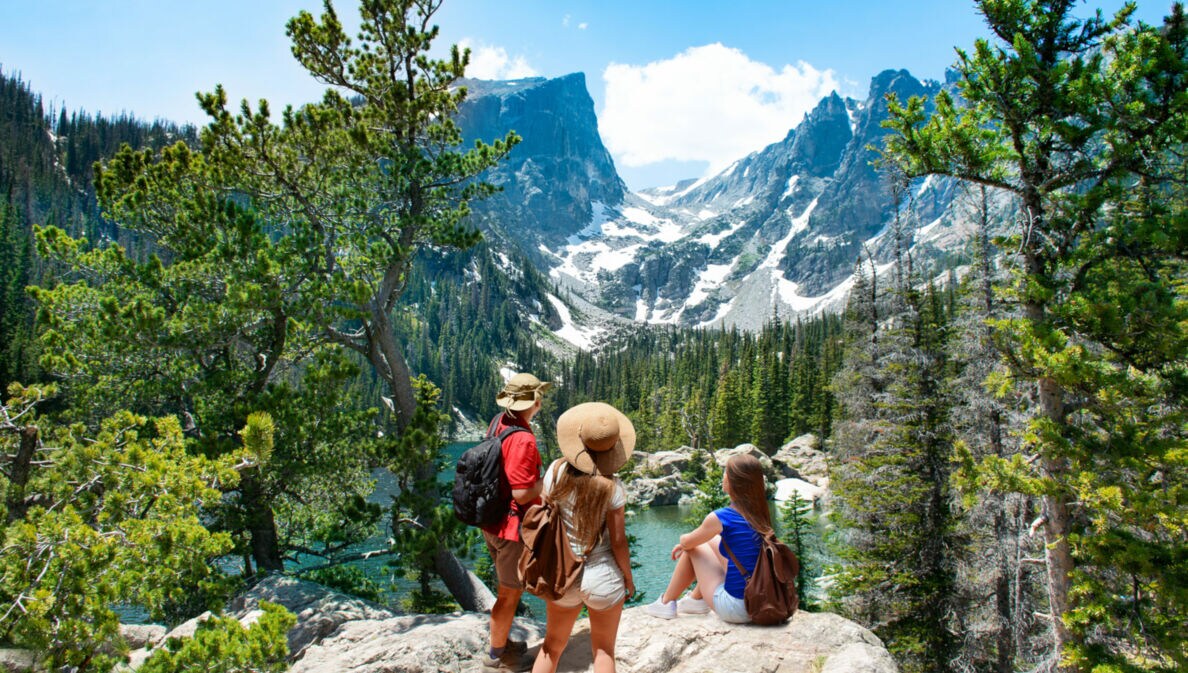 Drei Personen wandern durch die Rocky Mountains und blicken auf ein Bergpanorama.
