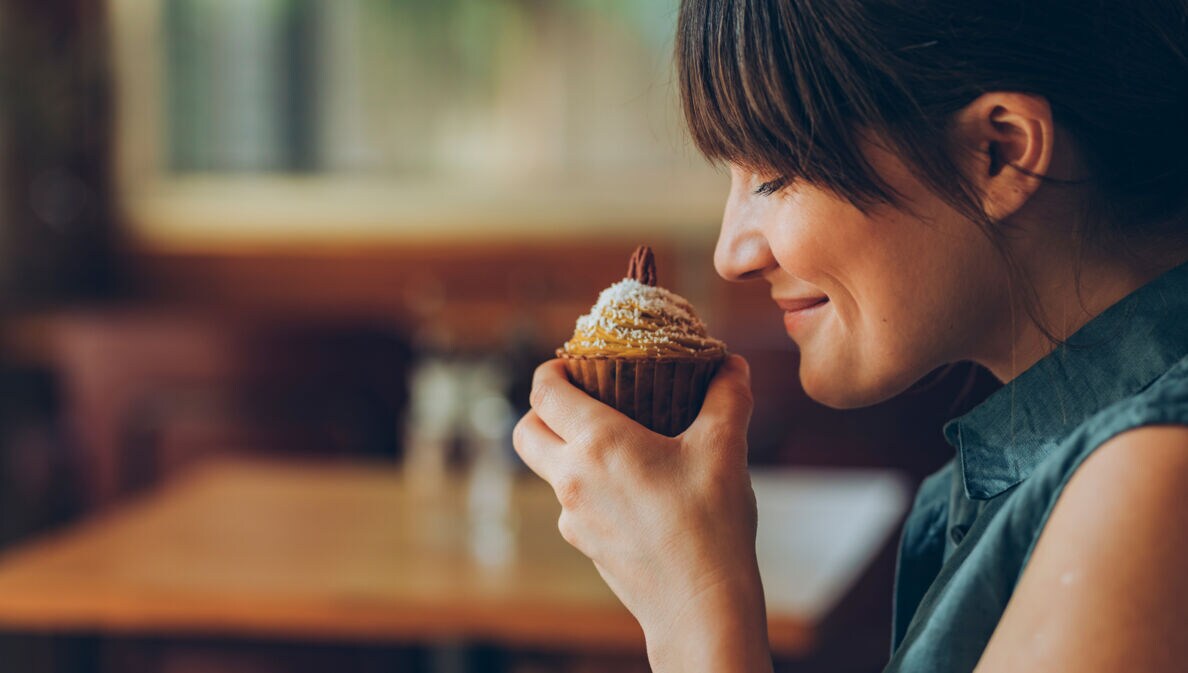 Eine Frau hält sich einen Nuss-Muffin an die Nase und lächelt, ihre Augen sind geschlossen.