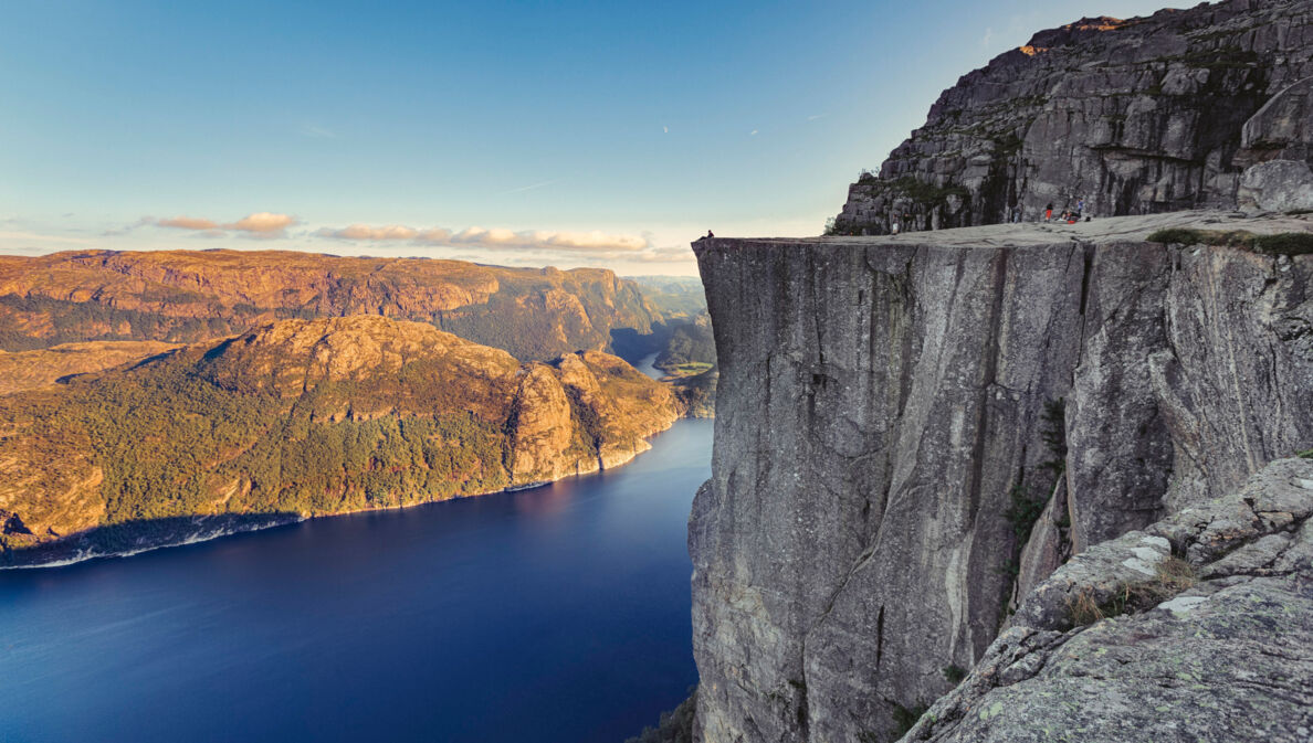 Fjordlandschaft an einem klaren Tag mit Personen auf einer beeindruckenden Felsklippe.