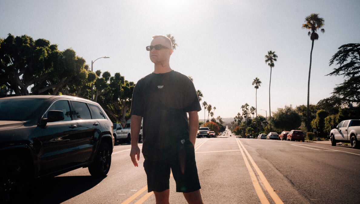 Benjamin Diedering posiert mit Sonnenbrille auf einer palmengesäumten Straße bei Sonnenschein.