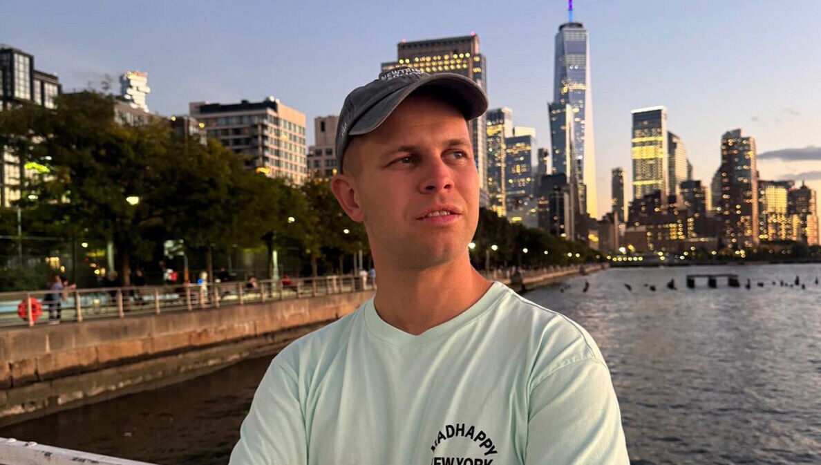 Porträt von Benjamin Diedering mit Baseballcap vor der Skyline New Yorks am Wasser.