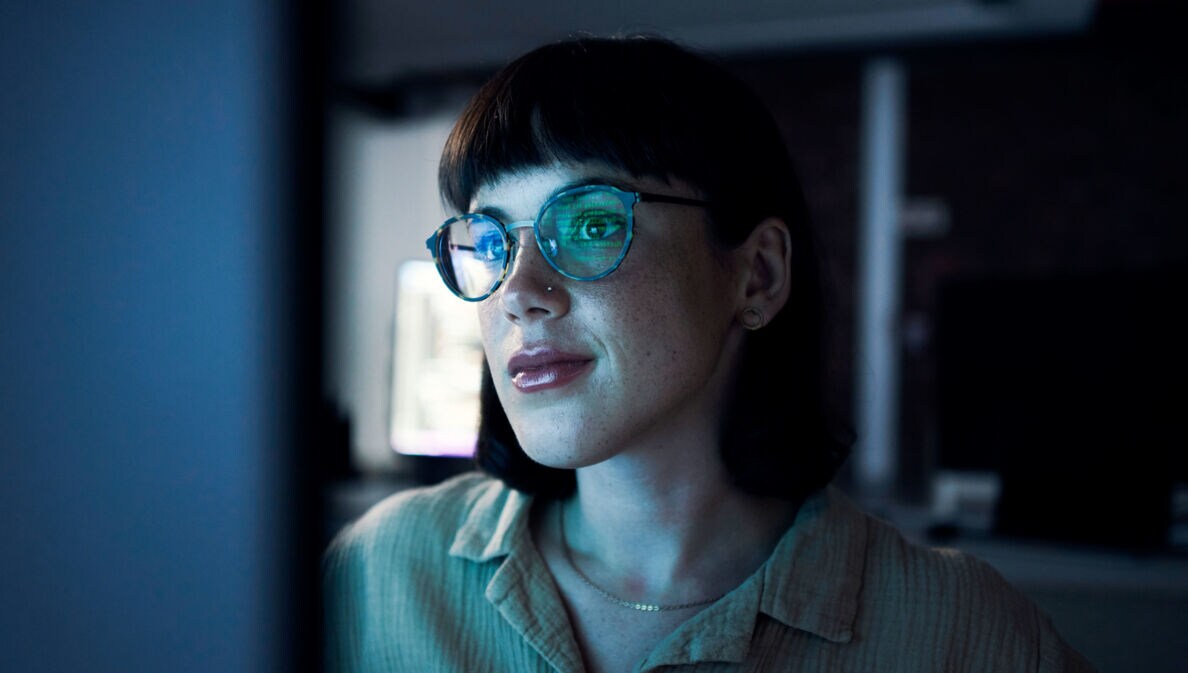 Eine Frau mit einer Brille in einem dunklen Raum vor einem Bildschirm.