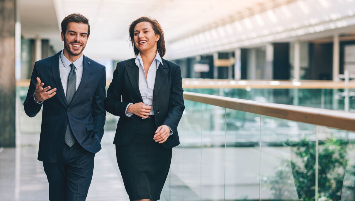 Ein Mann und eine Frau in formeller Business-Kleidung kommunizieren nebeneinander gehend.