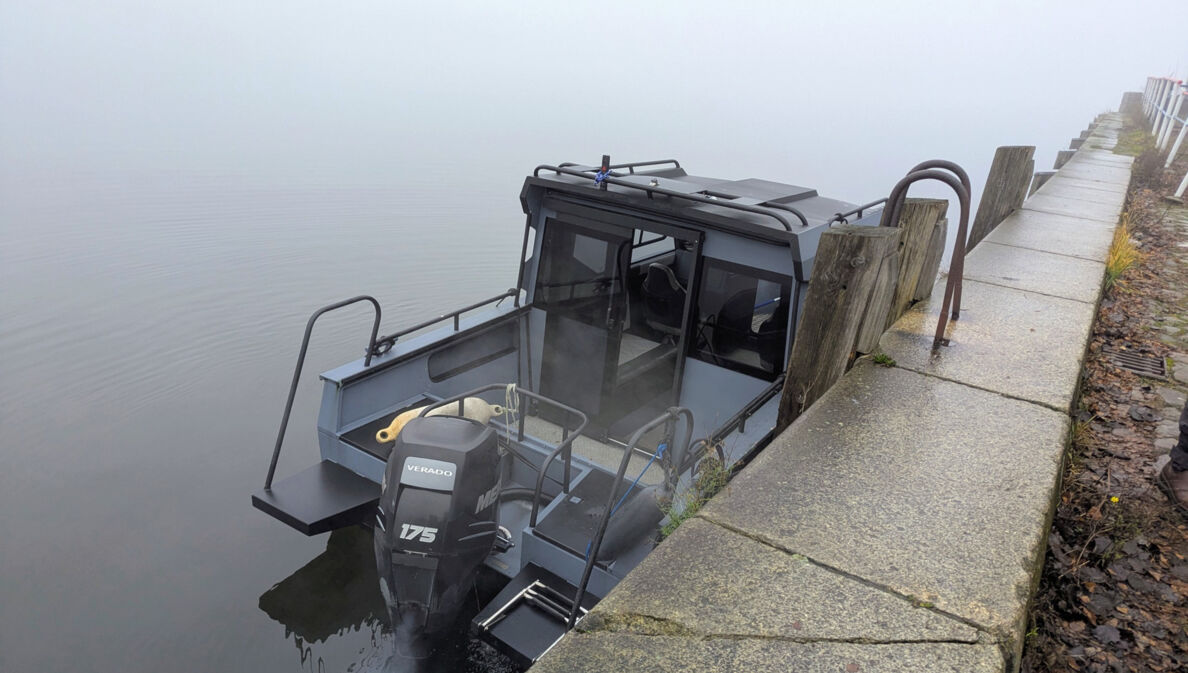 Ein Motorboot liegt bei dichtem Nebel an einer Kaimauer.
