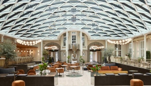 Hotellobby der Villa Copenhagen mit hoher, gläserner Decke und Loungemöbeln in Erdtönen.