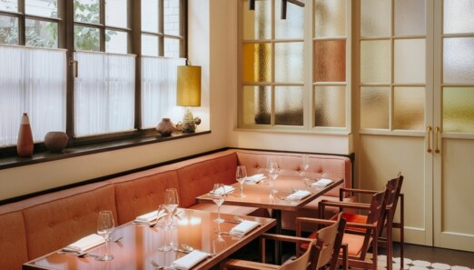 Interieur mit gedeckten Tischen und korallfarbenen Sitzmöbeln am Fenster.