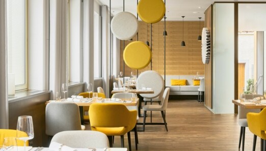 Helles stilvolles Interieur mit gelben und cremefarbenen Sitzmöbeln, dekorativer Trennwand und holzverkleideten Wänden.