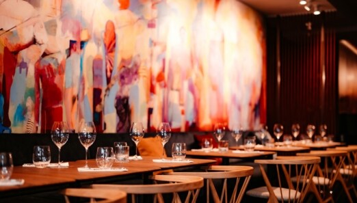 Mehrere eingedeckte Holztische vor einem bunten, großflächigem Wandbild.