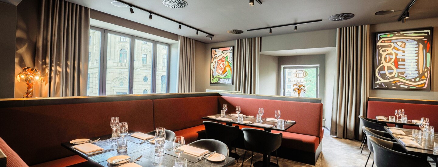 Blick in das Innere eines Restaurants mit eingedeckten Tischen und roten Sitzbänken.