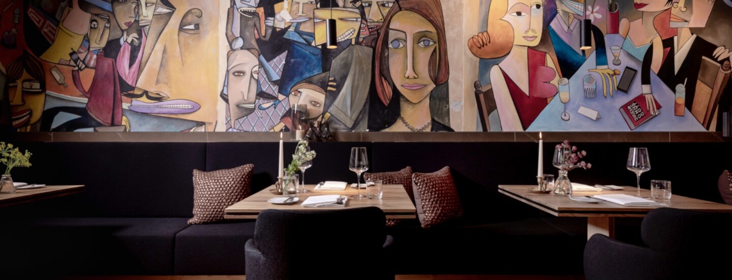 Tische und Bänke mit Kissen in einem Restaurant, an der Wand Malerei