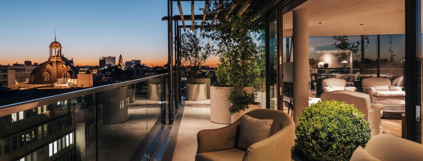 Dachterrasse mit hellen Polstermöbeln vor der Skyline Münchens bei Sonnenuntergang.