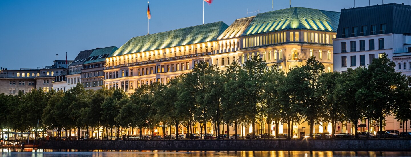 Beleuchtete Außenfassade des Hotels Vier Jahreszeiten am Wasser in der Dunkelheit.
