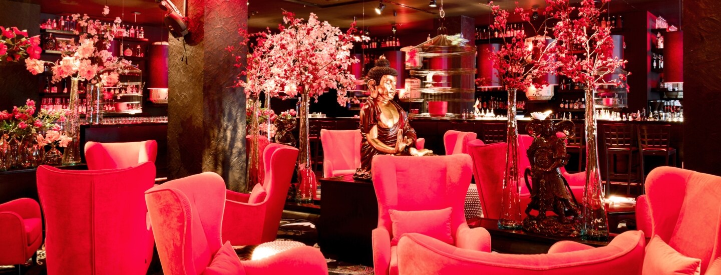 Beleuchtete, elegante Bar mit asiatischem Dekor und pinken Samtseseln.