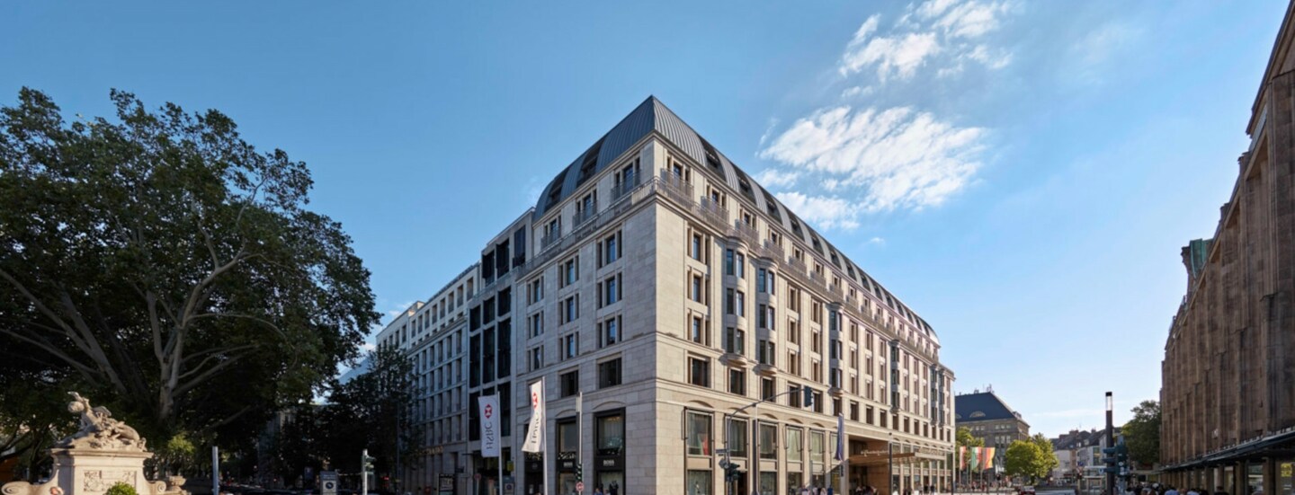 Eine helle Außenfassade des mehrstöckigen Gebäudes eines Luxushotels an einer Straßenkreuzung in Düsseldorf.