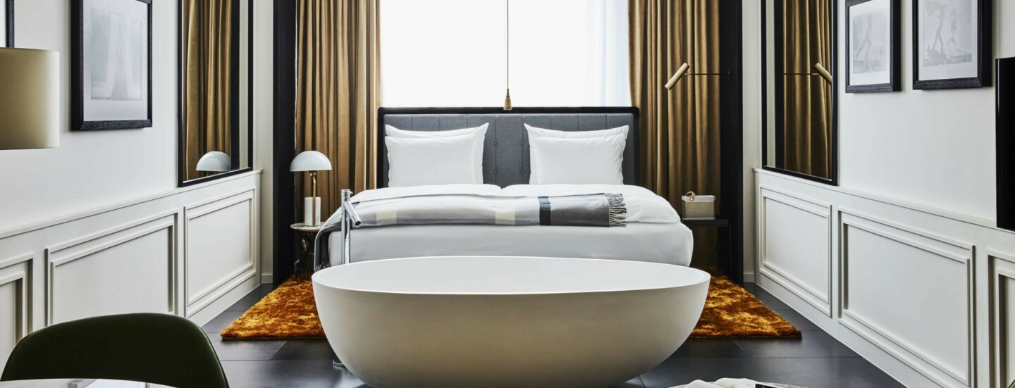 Moderne Hotelsuite mit einer freistehenden Badewanne vor einem Doppelbett.