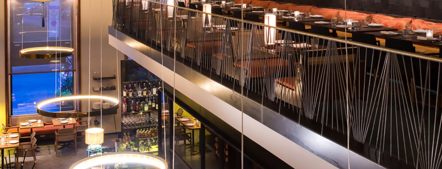 Modernes Restaurant mit hohen Decken und offener Galerie mit Sitzplätzen.