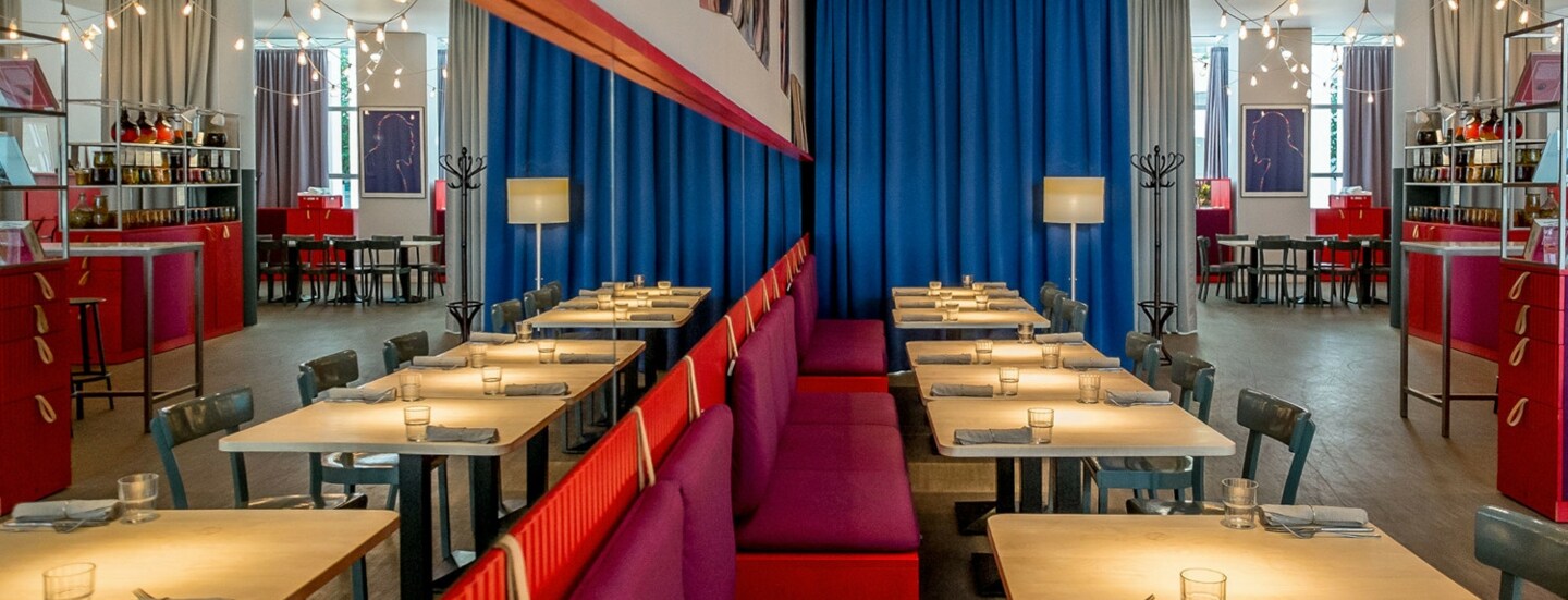 Modernes Restaurant mit hellen Holztischen und roten Sitzbänken an einer Spiegelwand.