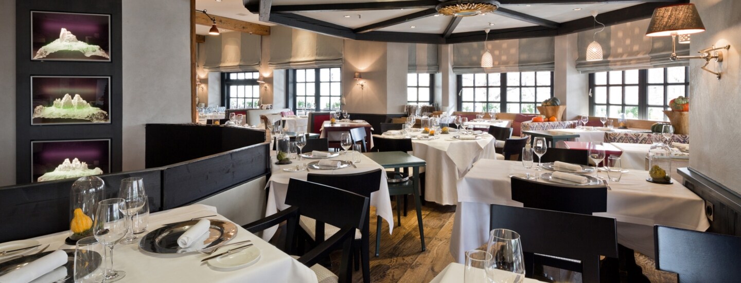 Elegantes Restaurant mit schwarzen Holzstühlen an eingedeckten Tischen mit weißen Tischdecken.