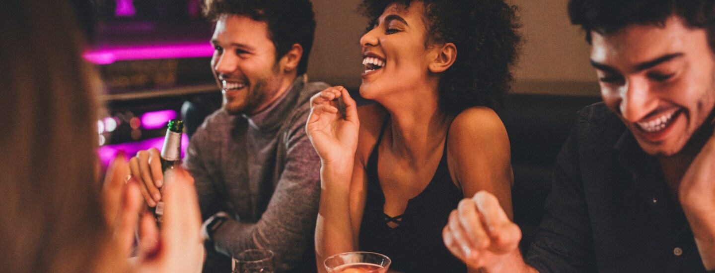 Eine Gruppe junger Menschen sitzt gut gelaunt mit Getränken an einem Tisch in einem Restaurant.