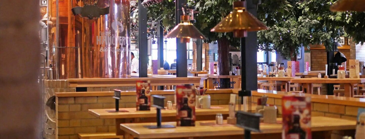 Gastronomiebereich in einem Brauhaus mit Holztischen und großem Kupferkessel.