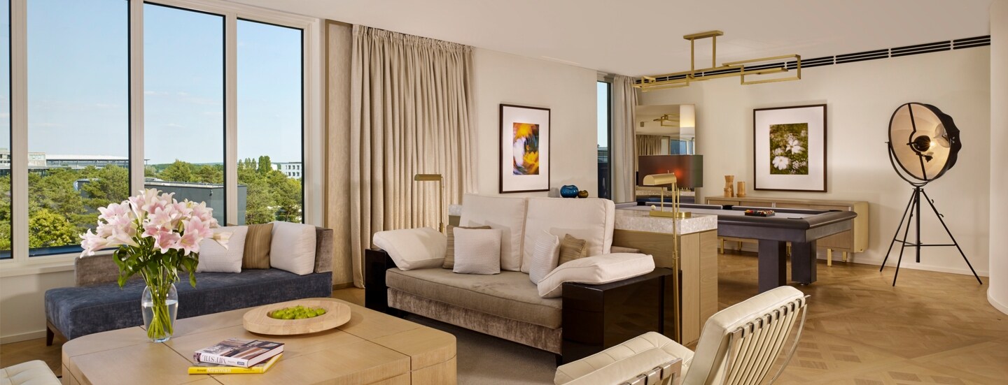 Eine modern und mit hellem Mobiliar eingerichtete Hotel-Suite mit großer Fensterfront.