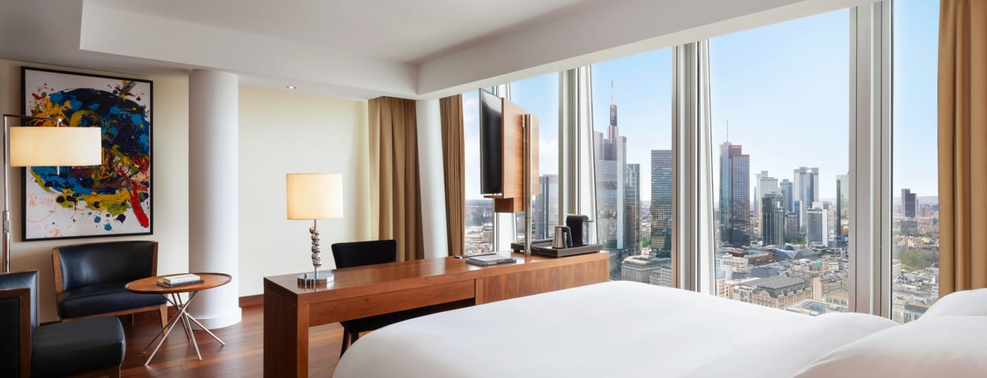 Modernes Hotelzimmer mit Blick auf die Frankfurter Skyline durch bodentiefe Panoramafenster.