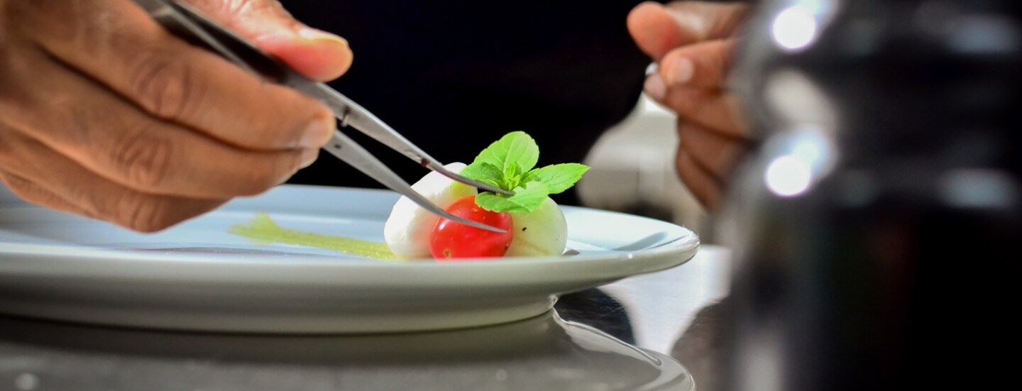 Eine Person richtet einen Teller sorgfältig mit einer Pinzette an.