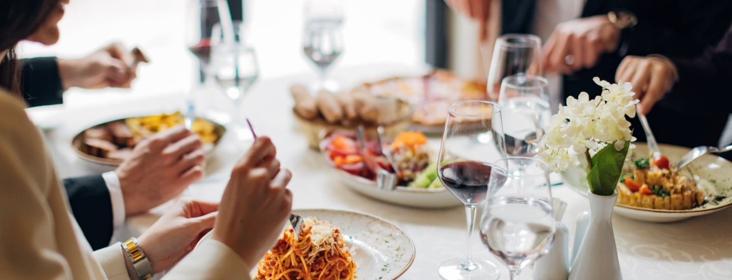 Eine Gruppe Personen an einem weiß eingedeckten Tisch in einem Restaurant mit verschiedenen Gerichten wie beispielsweise Pasta.