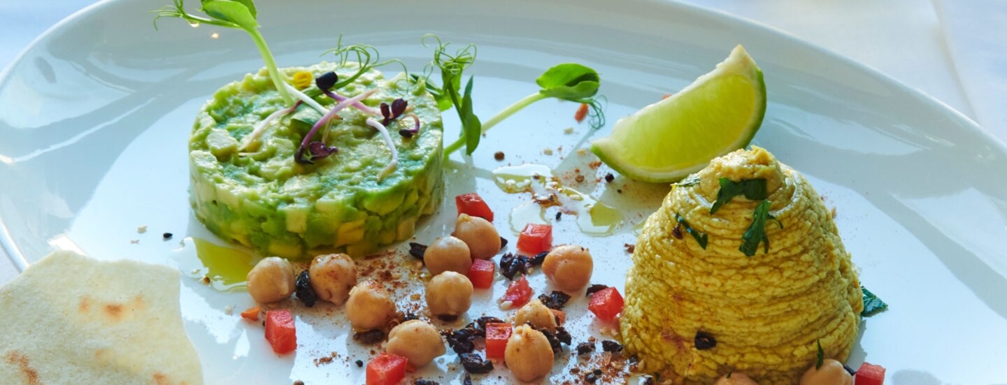 Ein weißer Porzellanteller mit einem Gericht aus Avocado, Kichererbsen, Limette und mehr im Restaurant brenner.