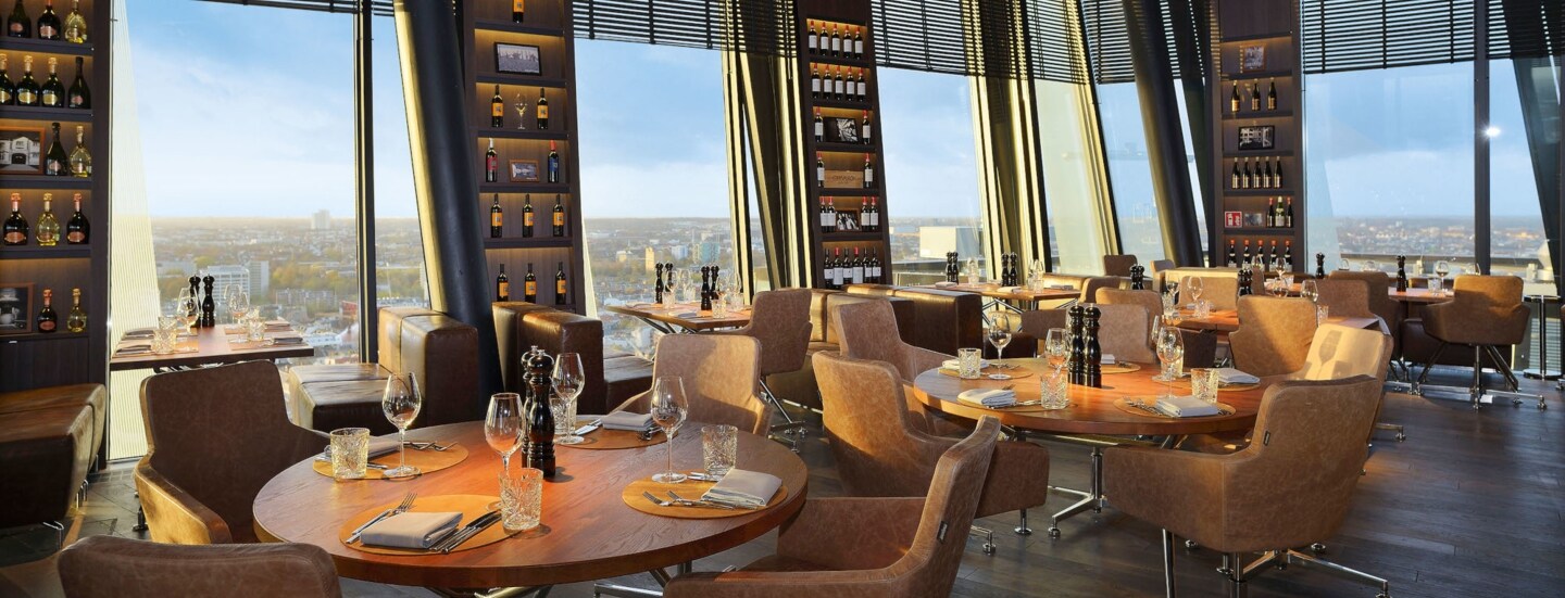 Das clouds Restaurant in Hamburg mit dunklem Ambiente, Ledersesseln, warmer Beleuchtung und runden Holztischen.