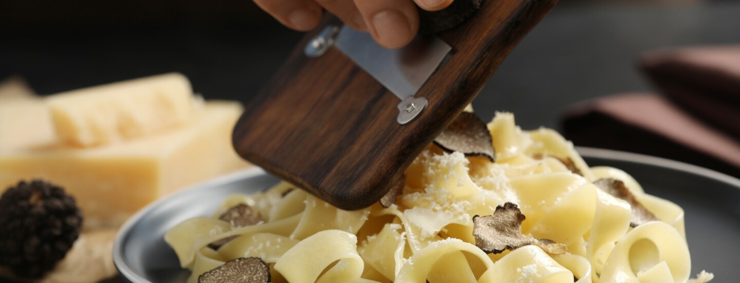 Nahaufnahme der Hand einer Person, die Trüffel auf einen Teller mit Nudeln hobelt.