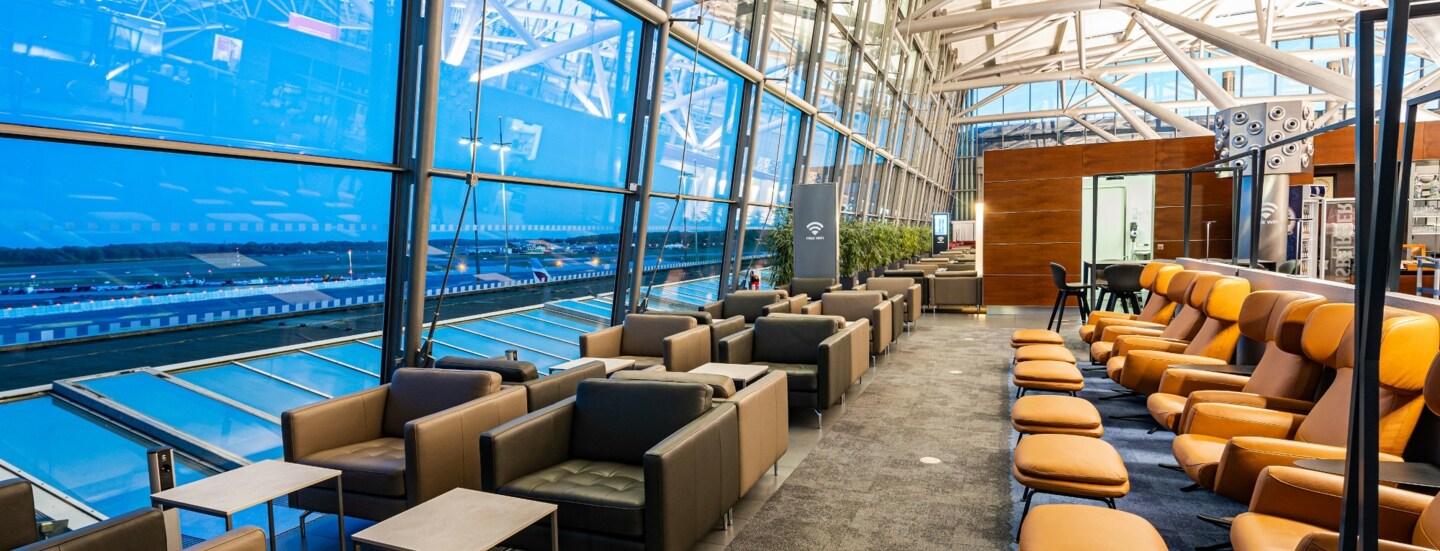 Eine Flughafenlounge mit Sitzgelegenheiten an Panoramafenstern.