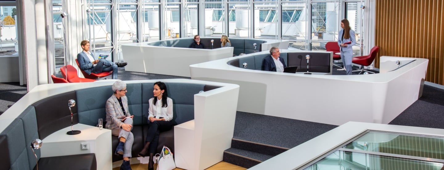Mehrere Personen sitzen in einer modernen Sitzlandschaft einer Flughafenlounge mit Panoramafenstern.