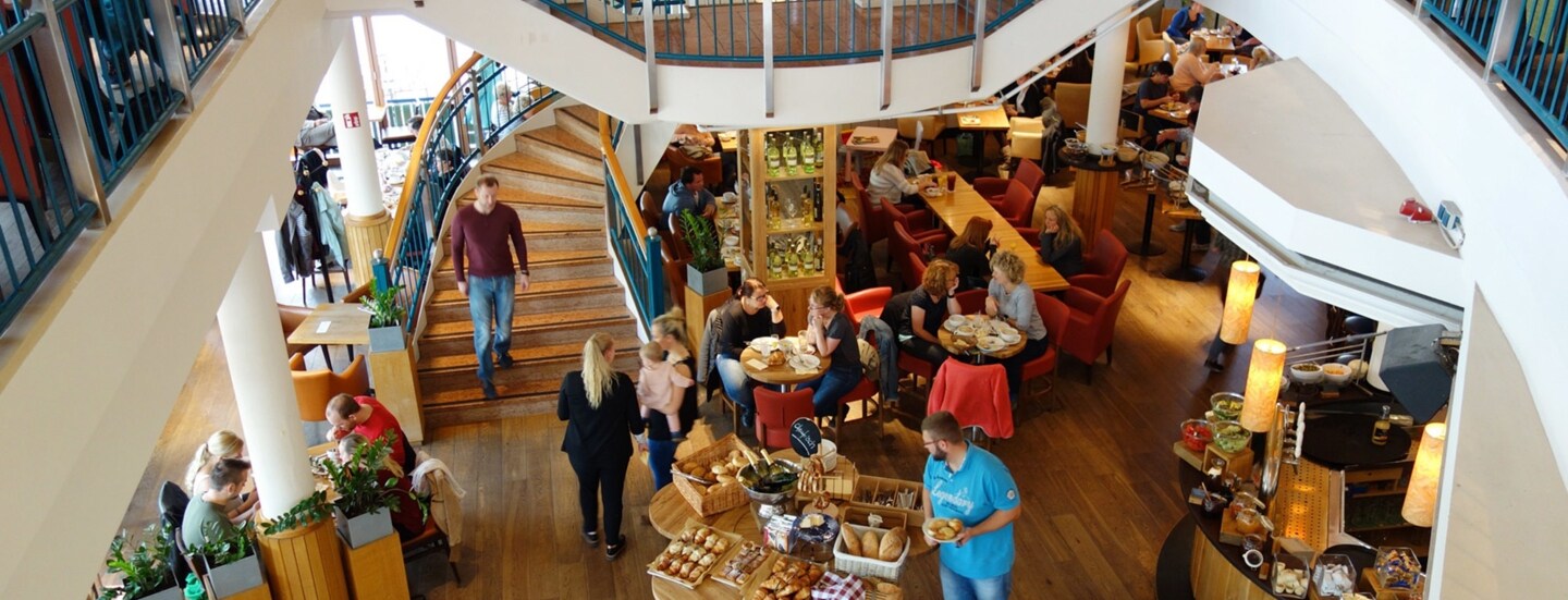 Aufsicht eines Innenraums in einem belebten Bistro mit Frühstücksbuffet.