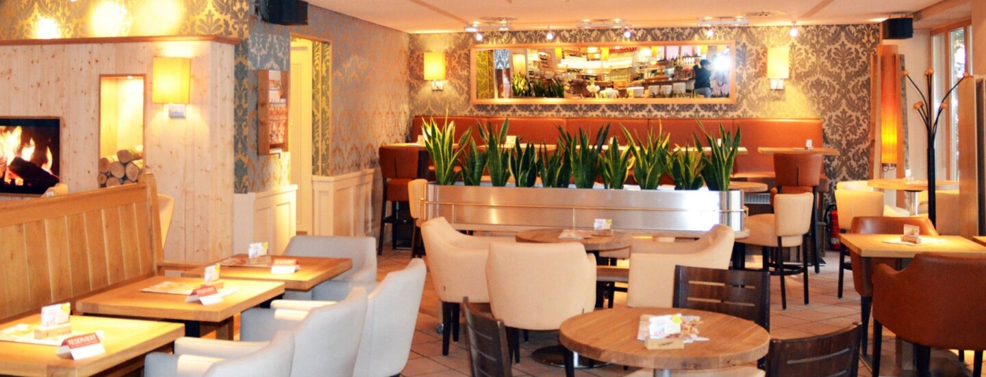 Ein Bistro mit Kamin und Mobiliar in Erdtönen bei warmer Beleuchtung.