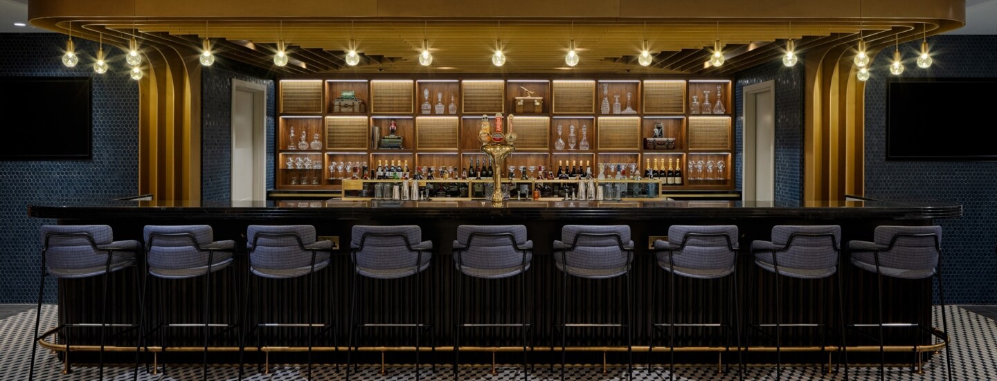 Stilvolle Bar mit goldenem Dekor und gepolsterten Barhockern am Tresen.