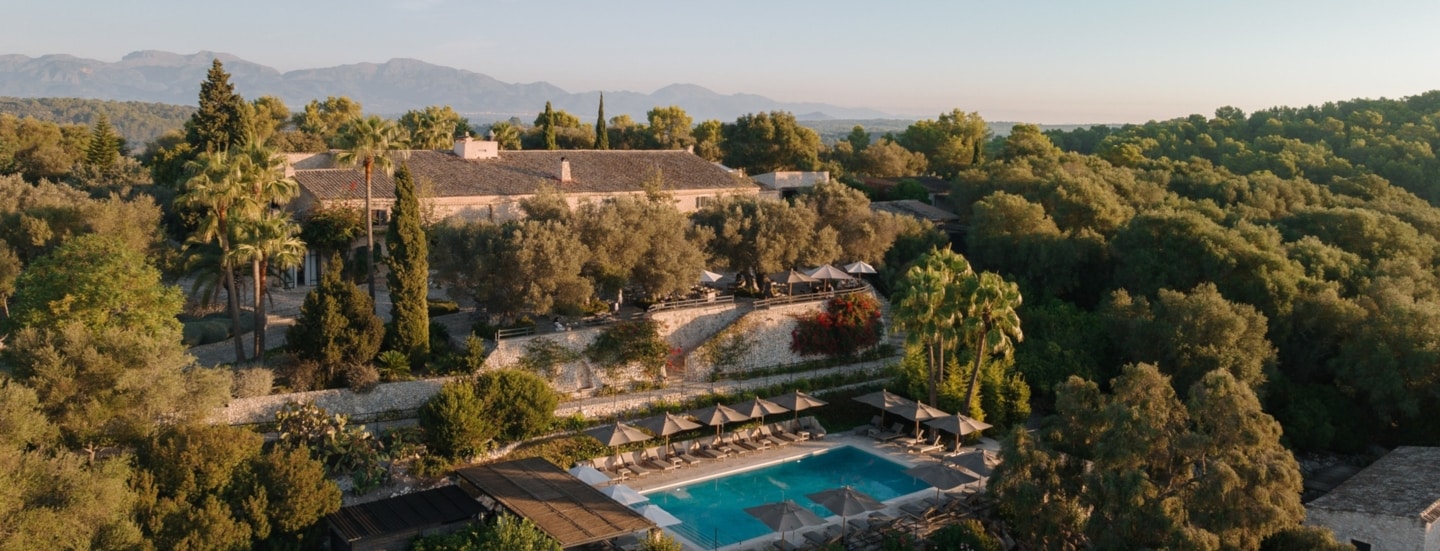 Luftaufnahme einer Finca mit Pool inmitten einer bewaldeten Hügellandschaft.