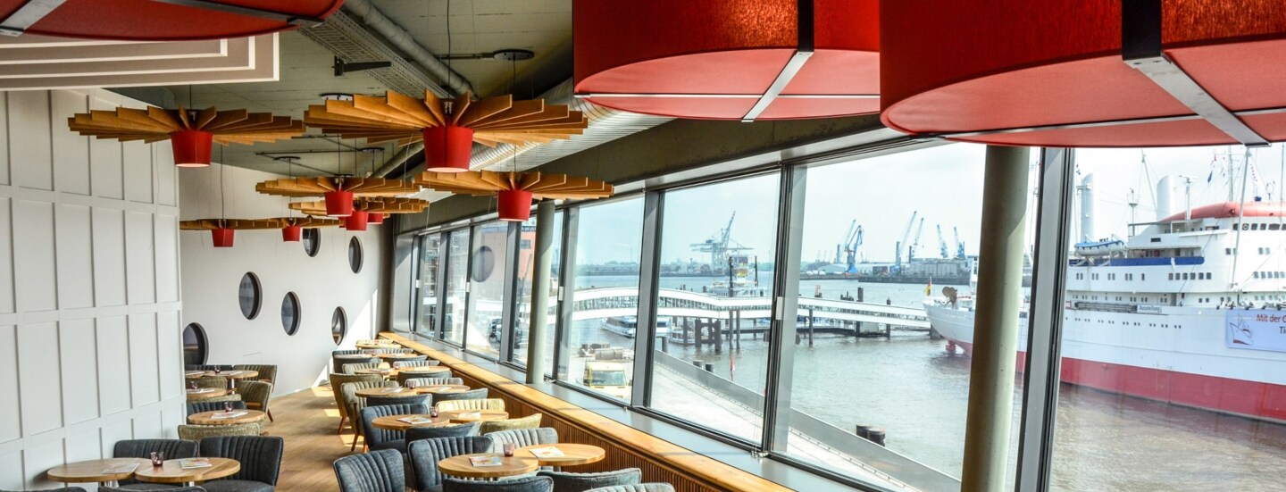 Modernes Bistro mit Blick auf den Hamburger Hafen durch Panoramafenster.