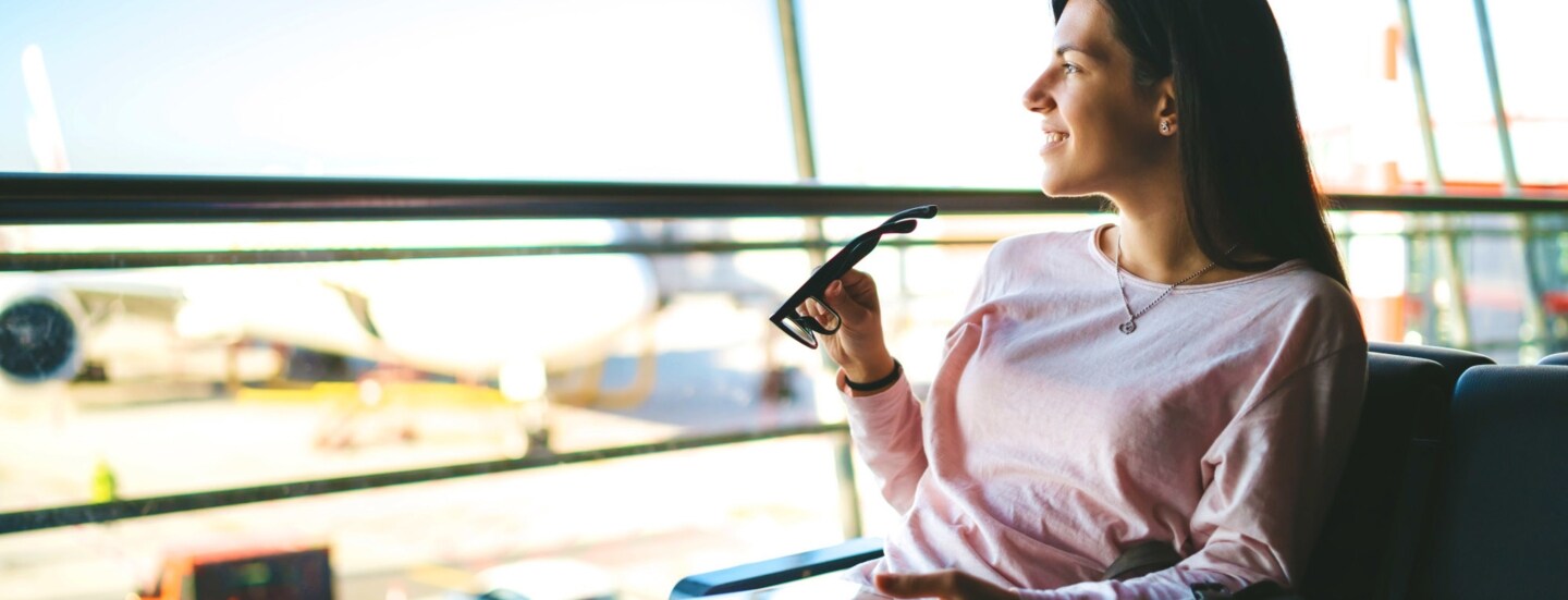 Eine Frau sitzt an einem Flugsteig und schaut aufs Vorfeld.