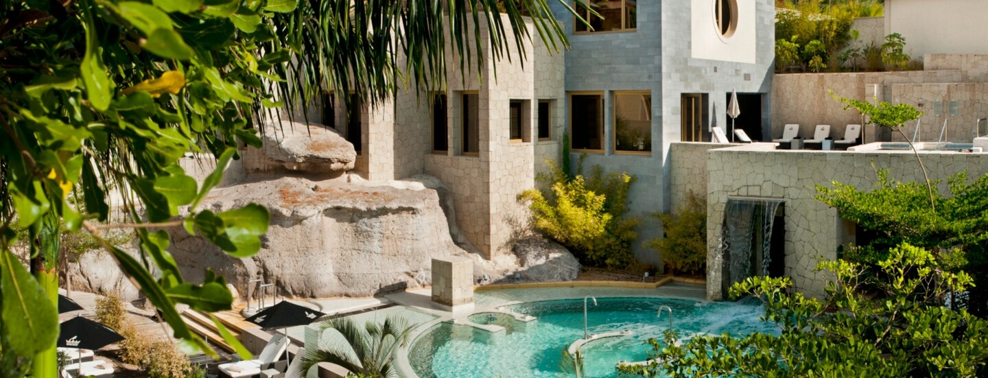 Resort des Bahia del Duque auf Teneriffa mit Poolanlage, Begrünung, Holzterrasse und Liegen.