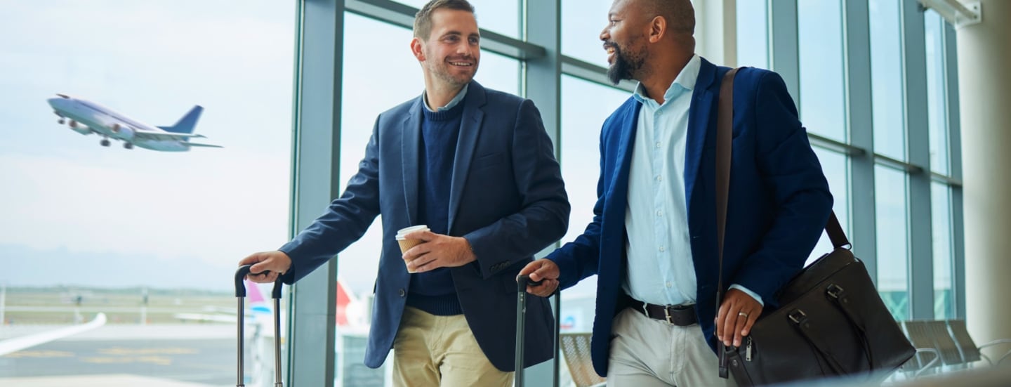 Zwei fröhliche Geschäftsmänner mit Trolleys an einem Flugsteig.