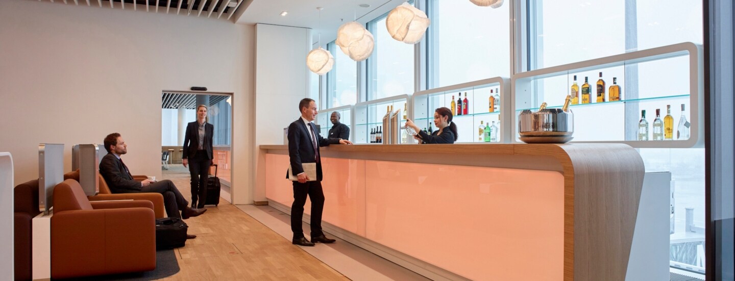 Personen in einer modernen Flughafenlounge mit Bar.