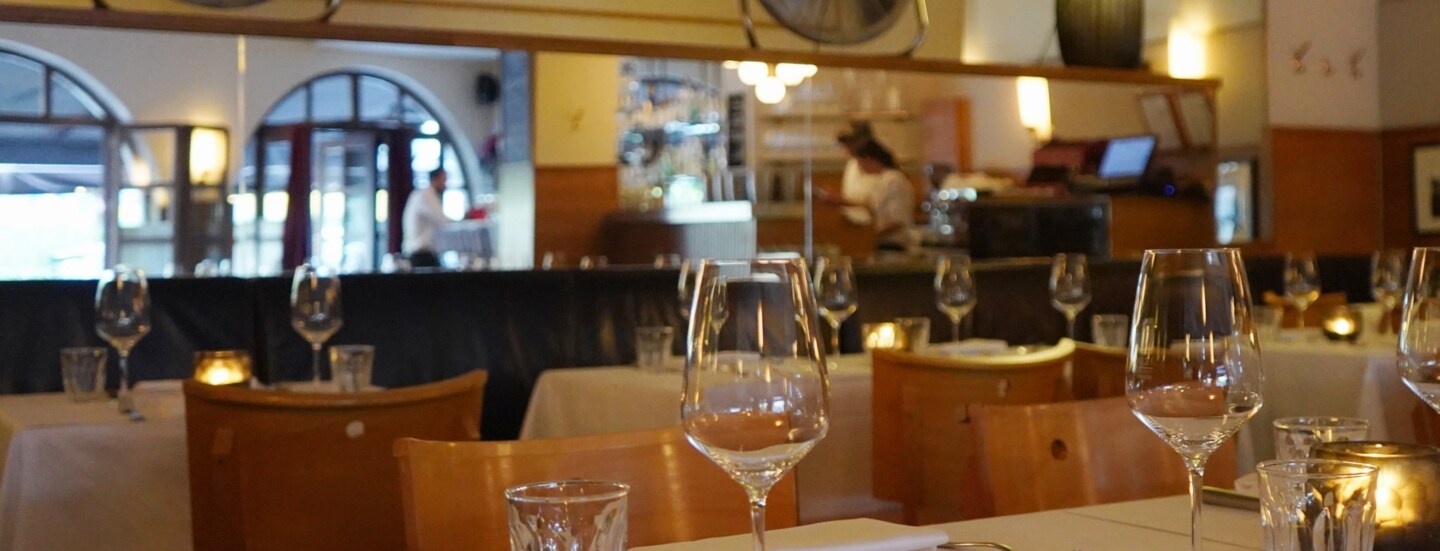 Speiseraum einer Brasserie mit eingedeckten Tischen bei gedimmtem Licht.