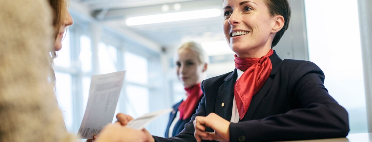 Eine Flugbegleiterin checkt Boardingpässe und begrüßt Reisende am Gate.
