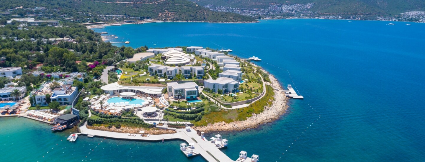 Luftaufnahme eines luxuriösen Hotelresorts mit weißen Bungalows auf einer Landzunge, umgeben von blauem Meer.