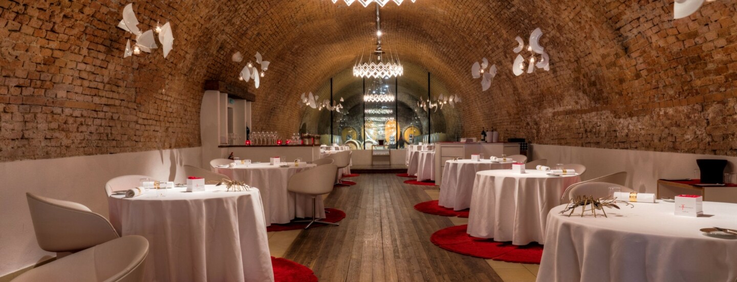 Speisesaal mit weiß eingedeckten, runden Tischen in einem Ziegelgewölbekeller.