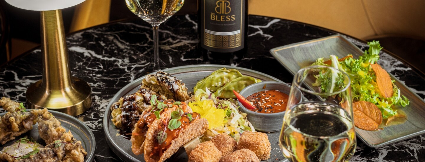 Ein gedeckter Tisch im Restaurant The Bless Berlin mit Wein und Tellern, auf denen kleine Happen liegen.